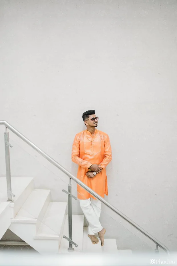 A client in an orange kurta against a white wall