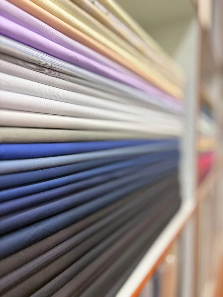 Close-up of suiting fabrics stacked on edge, colours receding into shallow focus